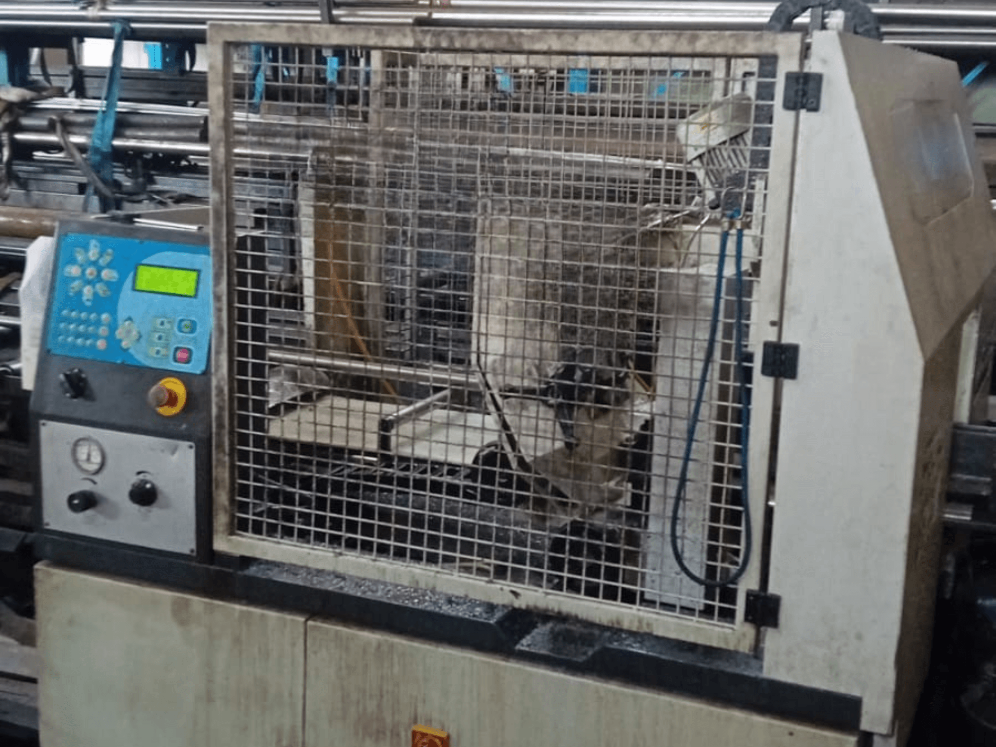 Metāla lentzāģis Macc 381 AV, skats no priekšpuses, redzams vadības panelis, drošības būris un metāla izstrādājumu atliekas uz pamatnes.