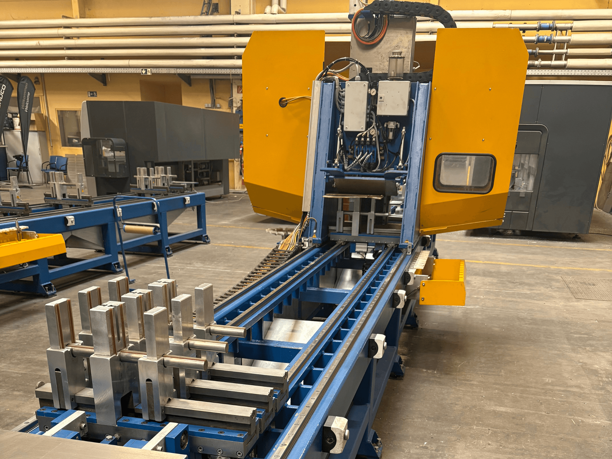 SCHÜCO PBX AL universālā apstrādes centra priekšējais skats, kurā uz zilas apstrādes gultnes redzamas metāla sagataves.