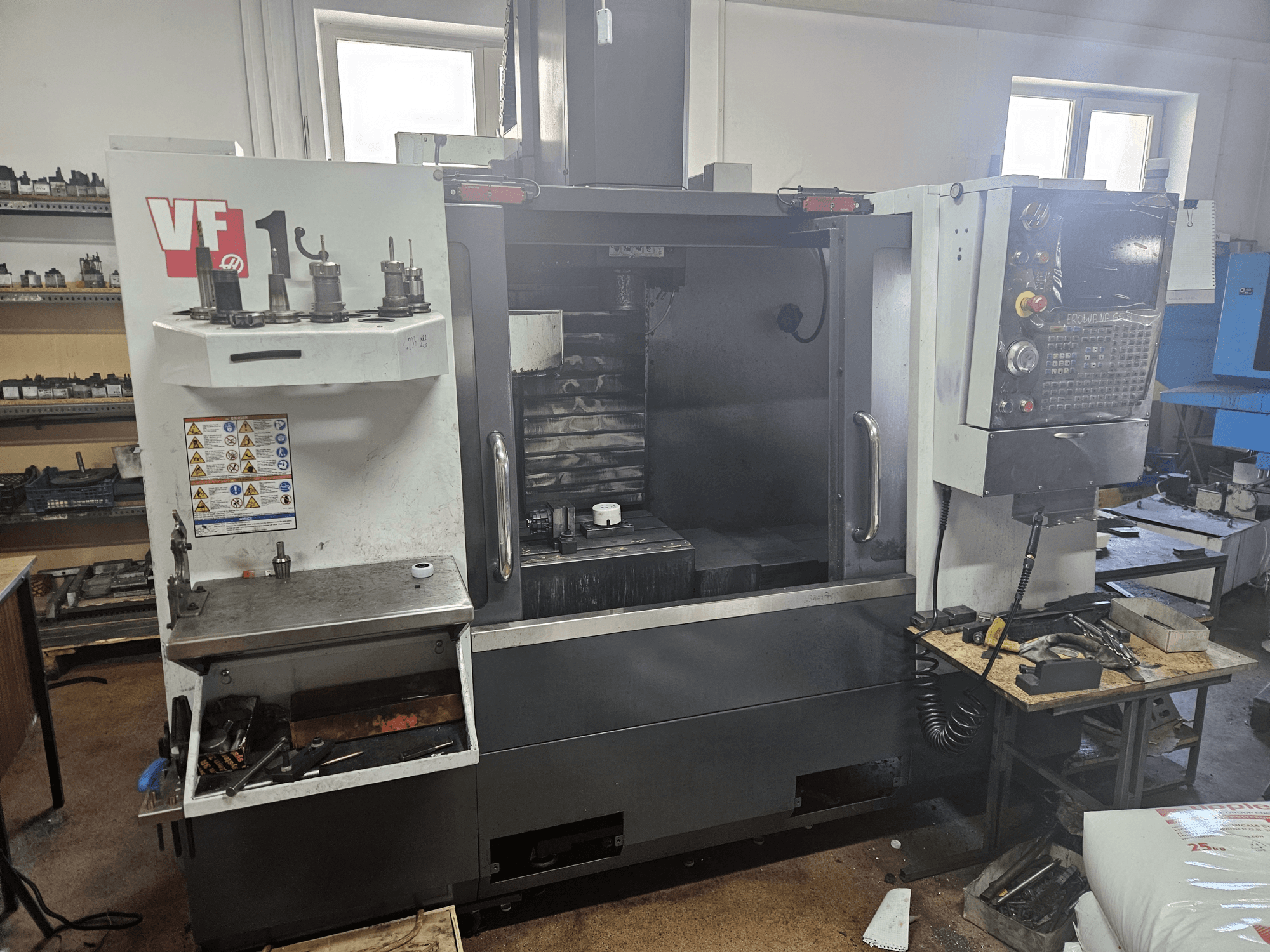 HAAS VF-1 vertikālais apstrādes centrs, skats no priekšpuses ar instrumentiem sānos, redzams vadības panelis un darba zona fonā.
