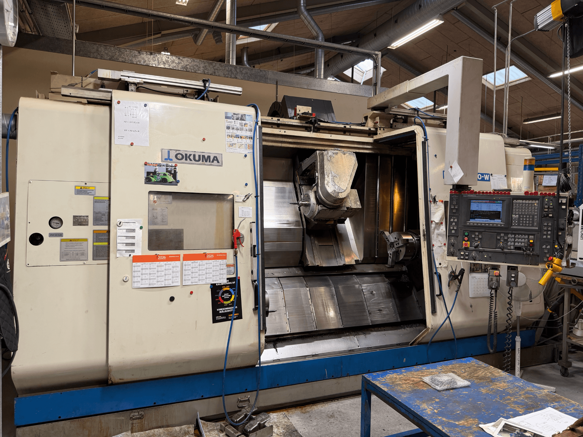 Okuma MacTurn350-W virpošanas-frēzēšanas centrs, skats no priekšpuses, kurā redzams vadības panelis un brīva piekļuve apstrādes zonai.