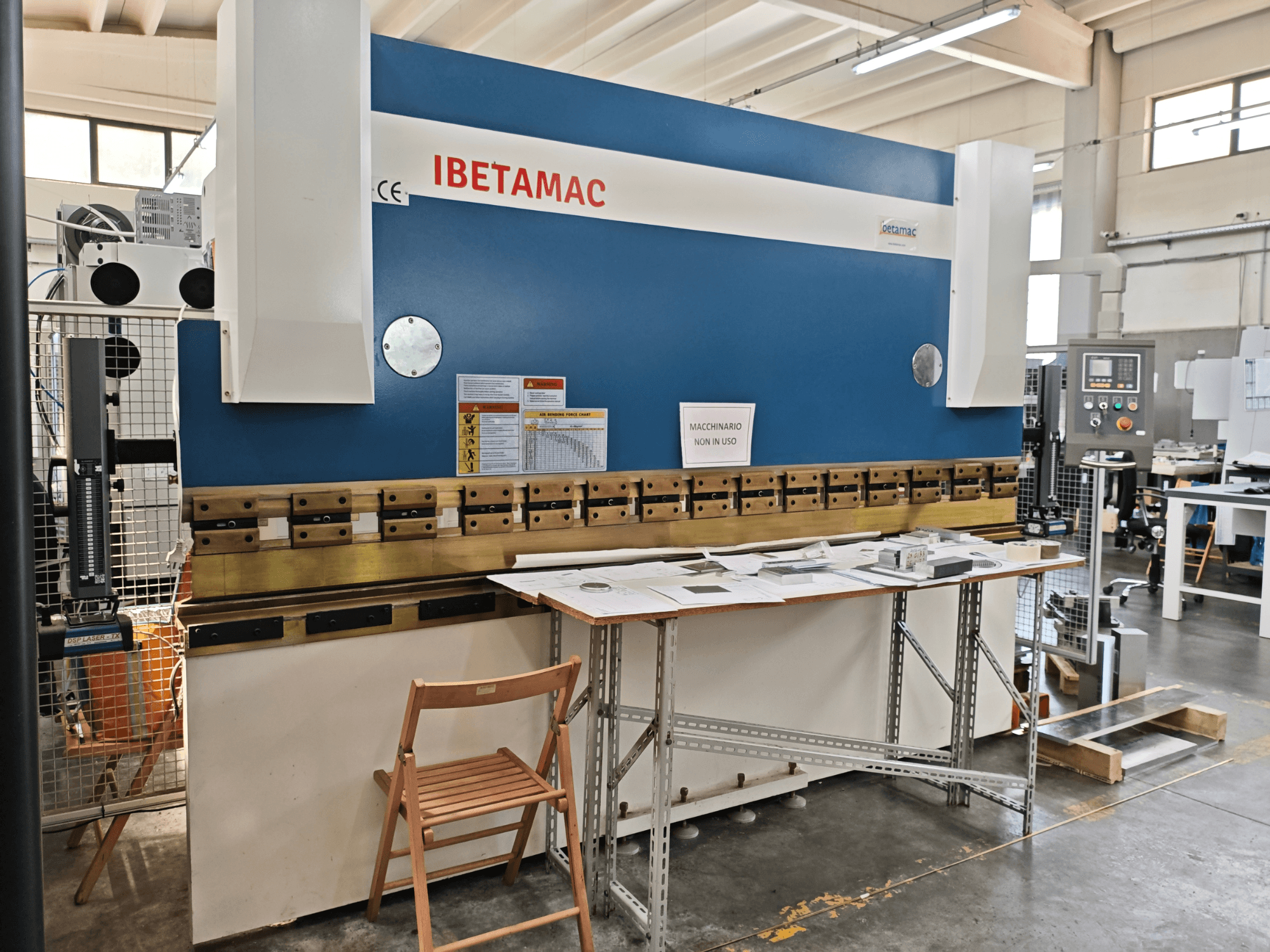 IBETAMAC 3200 100T lieces preses darbnīcā, sānskats, kurā redzams vadības panelis, darba zona un drošības norādes.