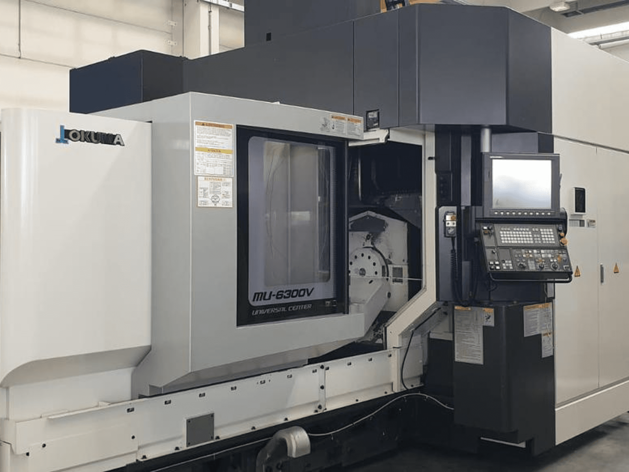 Okuma MU 6300 V vertikālais apstrādes centrs, priekšējais skats, kurā redzams vadības panelis un apstrādes zonas detaļas.