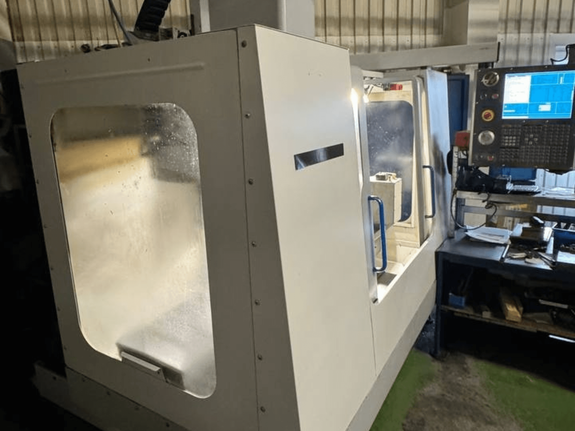 HAAS VCE 750 vertikālais apstrādes centrs sānu skatā, ar vadības paneli un caurspīdīgu drošības korpusi.