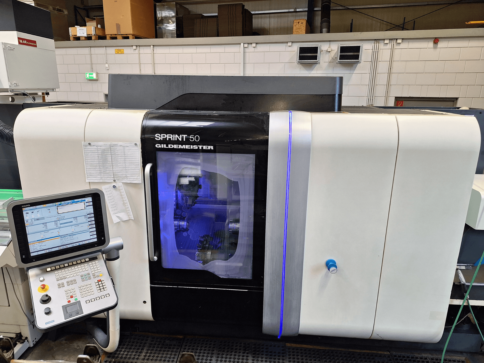 DMG Sprint 50 2T horizontālās virpošanas iekārta, skats no priekšpuses, ar vadības paneli un caurspīdīgu korpusu, kas parāda iekārtas iekšpusē.