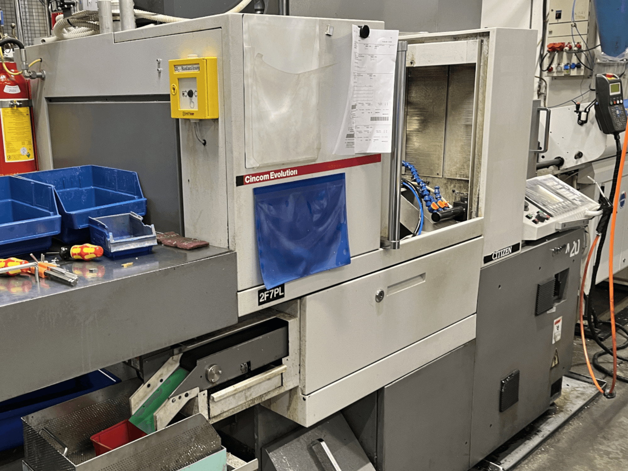 Cincom Evolution 2F7PL apstrādes centrs, skats no priekšpuses; vadības ierīces, instrumentu tvertnes un detalizēts vadības panelis.