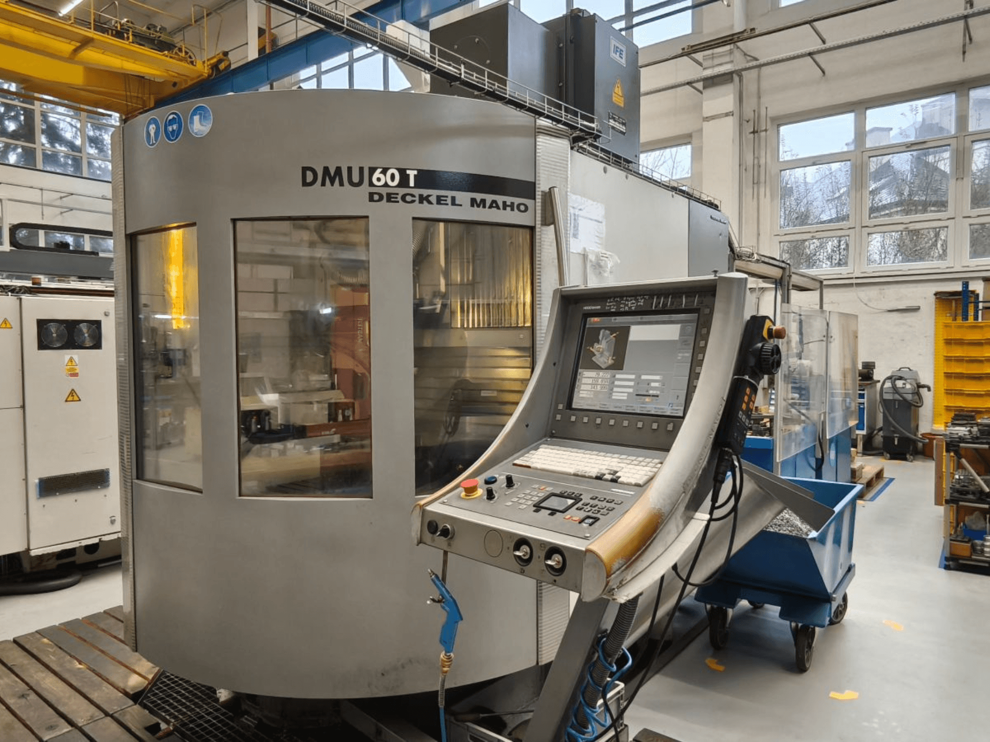 DECKEL MAHO DMU 60T apstrādes centra ar vadības paneli vertikāls skats, uz kura redzami precīzijas instrumenti darbnīcā.