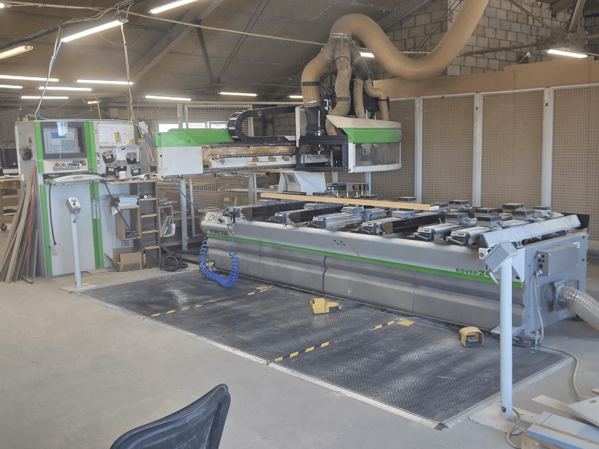 CNC apstrādes centrs BIESSE Rover 24S darbnīcā ar vadības paneli un lielu darba virsmu ar koka detaļām.