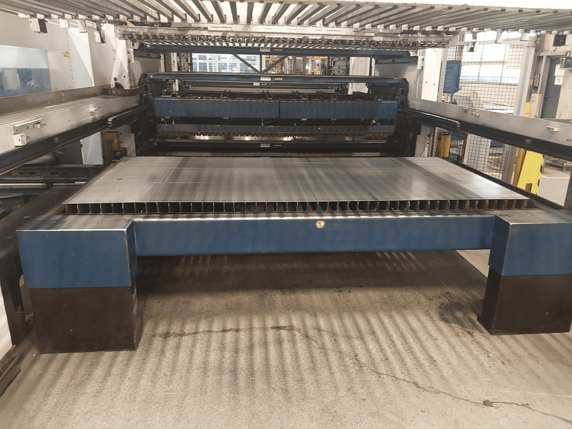 TRUMPF TruLaser 3030 L20 CO2 lāzera griešanas mašīnas TRUMPF TruLaser 3030 L20 priekšējais skats ar lielu griešanas gultni un atbalsta struktūru.