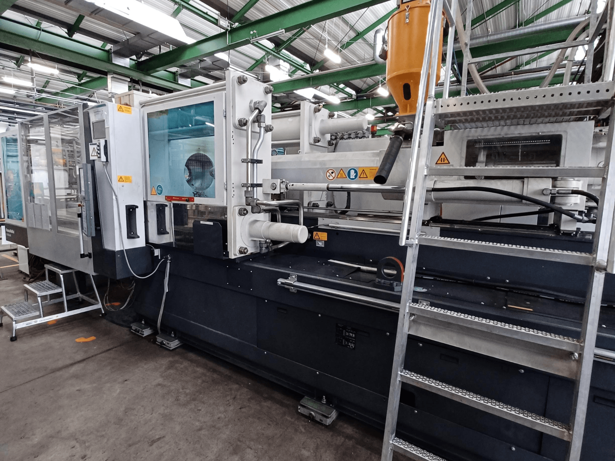 Rūpnieciskā liešanas mašīna ar skaidru priekšējo skatu, kurā redzami zīmola marķējumi, vadības panelis un materiālu tvertne.