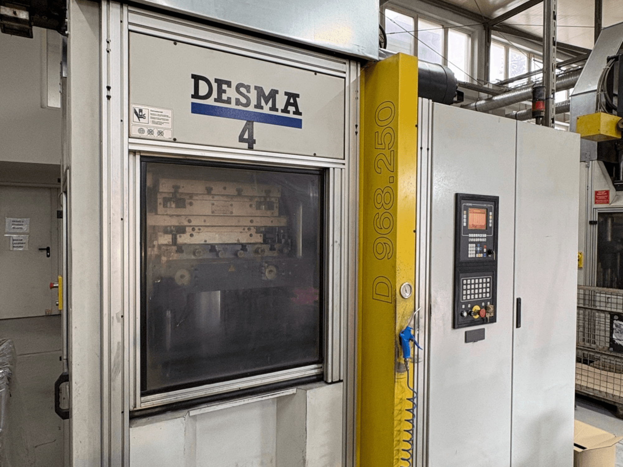 Vertikālā iesmidzināšanas iekārta Kloeckner Desma 968.250, priekšējais skats, kurā redzams vadības panelis un iekārtas detaļas.