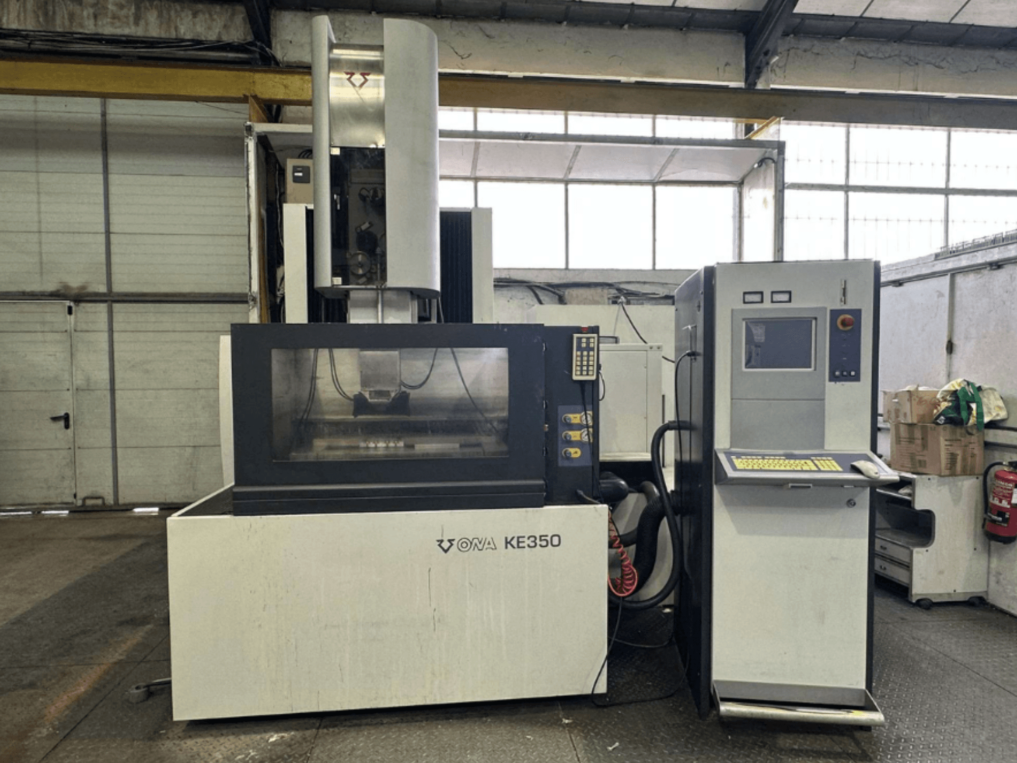 ONA KE350 CNC mašīnas priekšējais skats ar vadības paneli, displeja ekrānu un dažādām pogām, kas atrodas rūpnieciskā vidē.