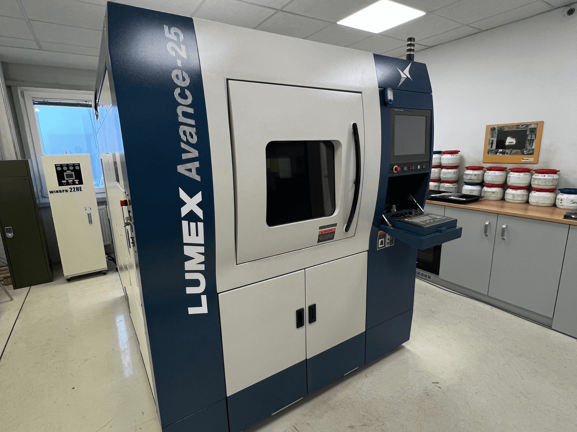 LUMEX Avance-25 3D printeris laboratorijā, skats no priekšpuses. Vadības panelis ar redzamu ekrānu un pogām, iekārtas fonā.