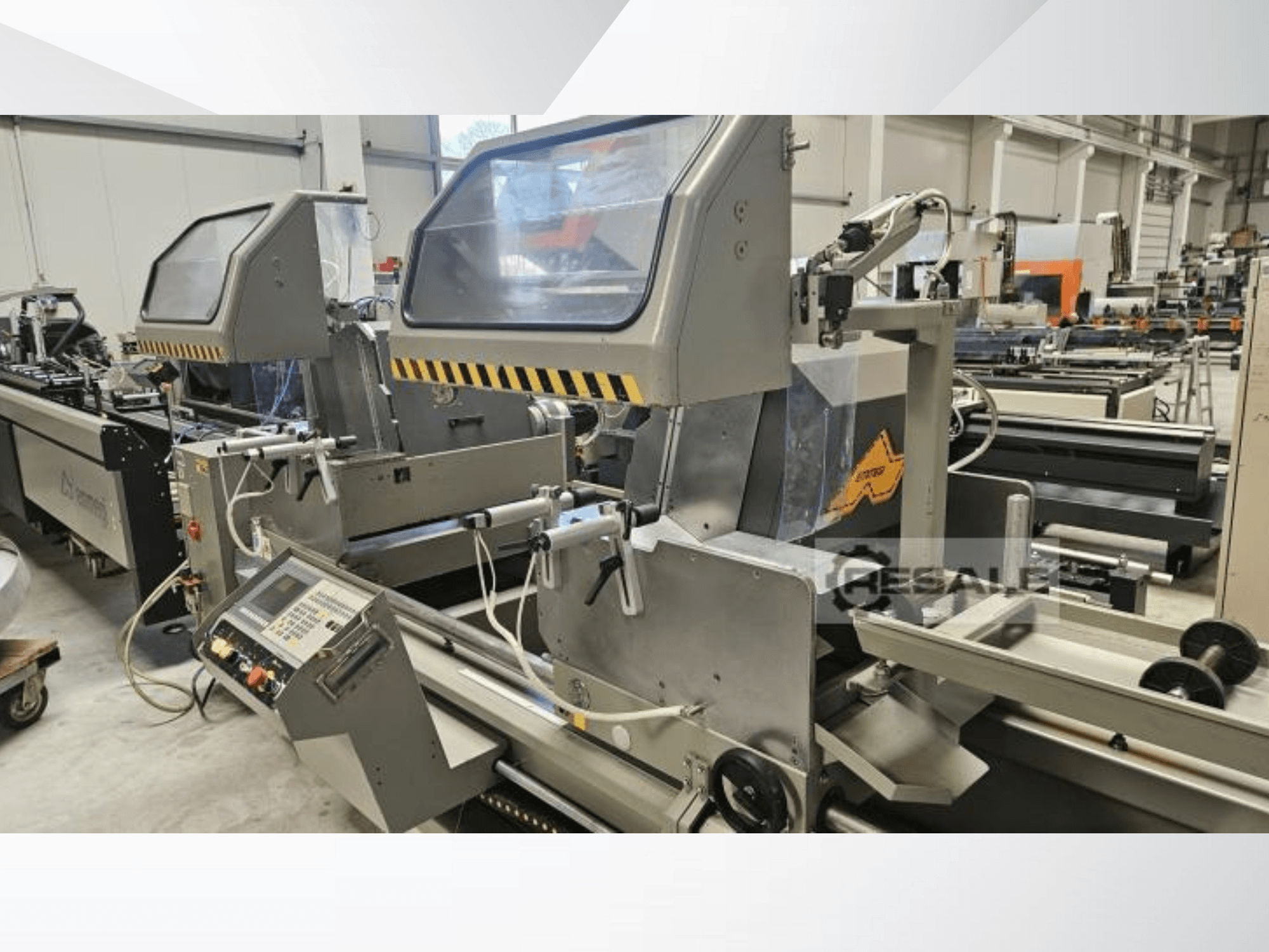 Dubultā zāģēšanas iekārta rūpnīcā; priekšējais skats, kurā redzams vadības panelis, stikla pārsegi un griešanas komponenti.