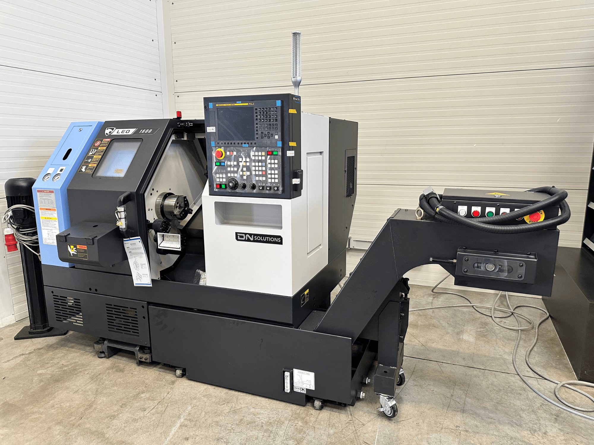 Priekšējais skats uz DN SOLUTIONS Leo 1600 virpošanas frēzēšanas centru ar digitālo vadības paneli un instrumentu turētāju uz melnas pamatnes.