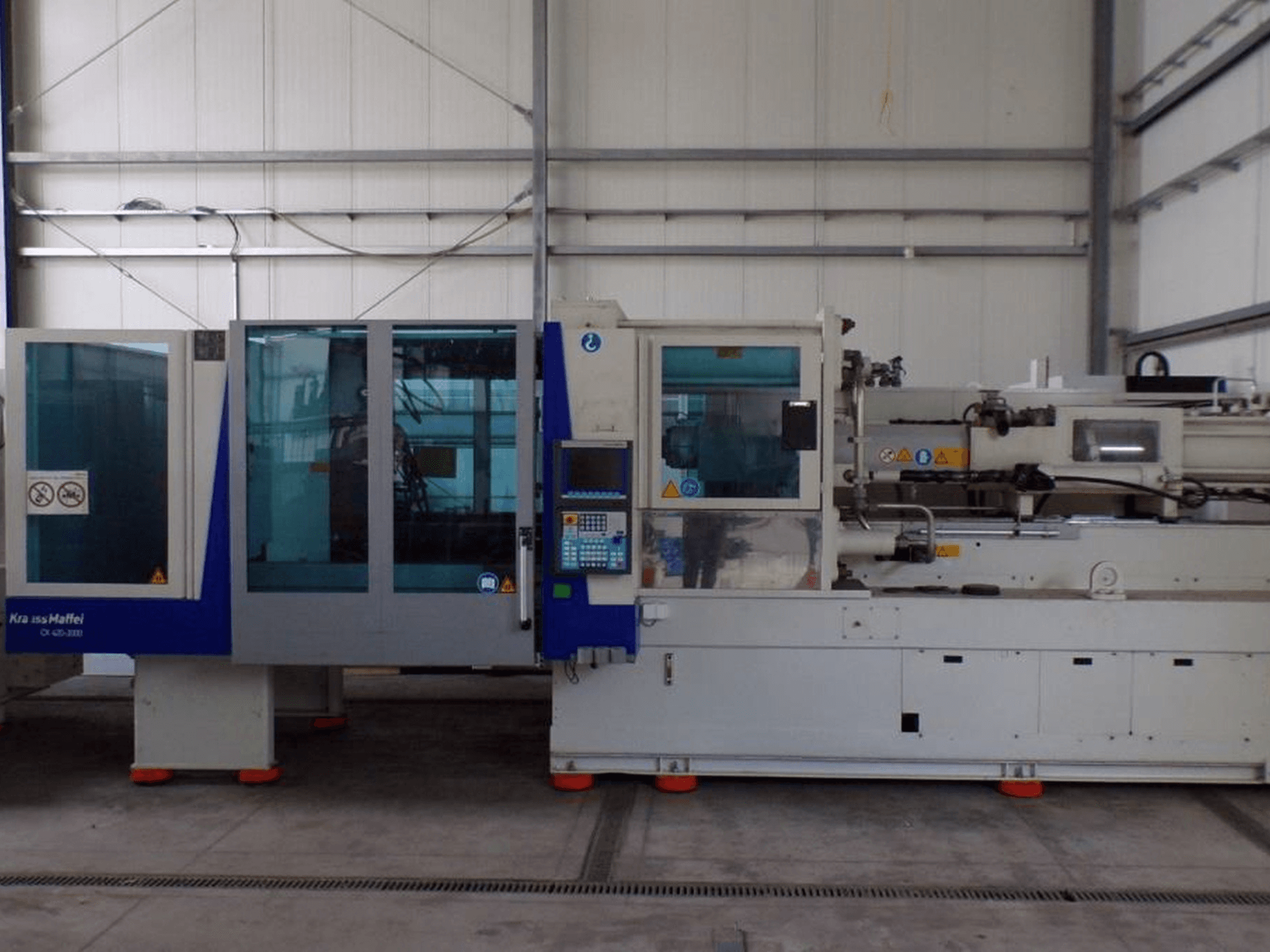 KraussMaffei iesmidzināšanas veidošanas iekārta, skats no sāniem, ar vadības paneli un drošības indikatoriem, redzama rūpnīcā.