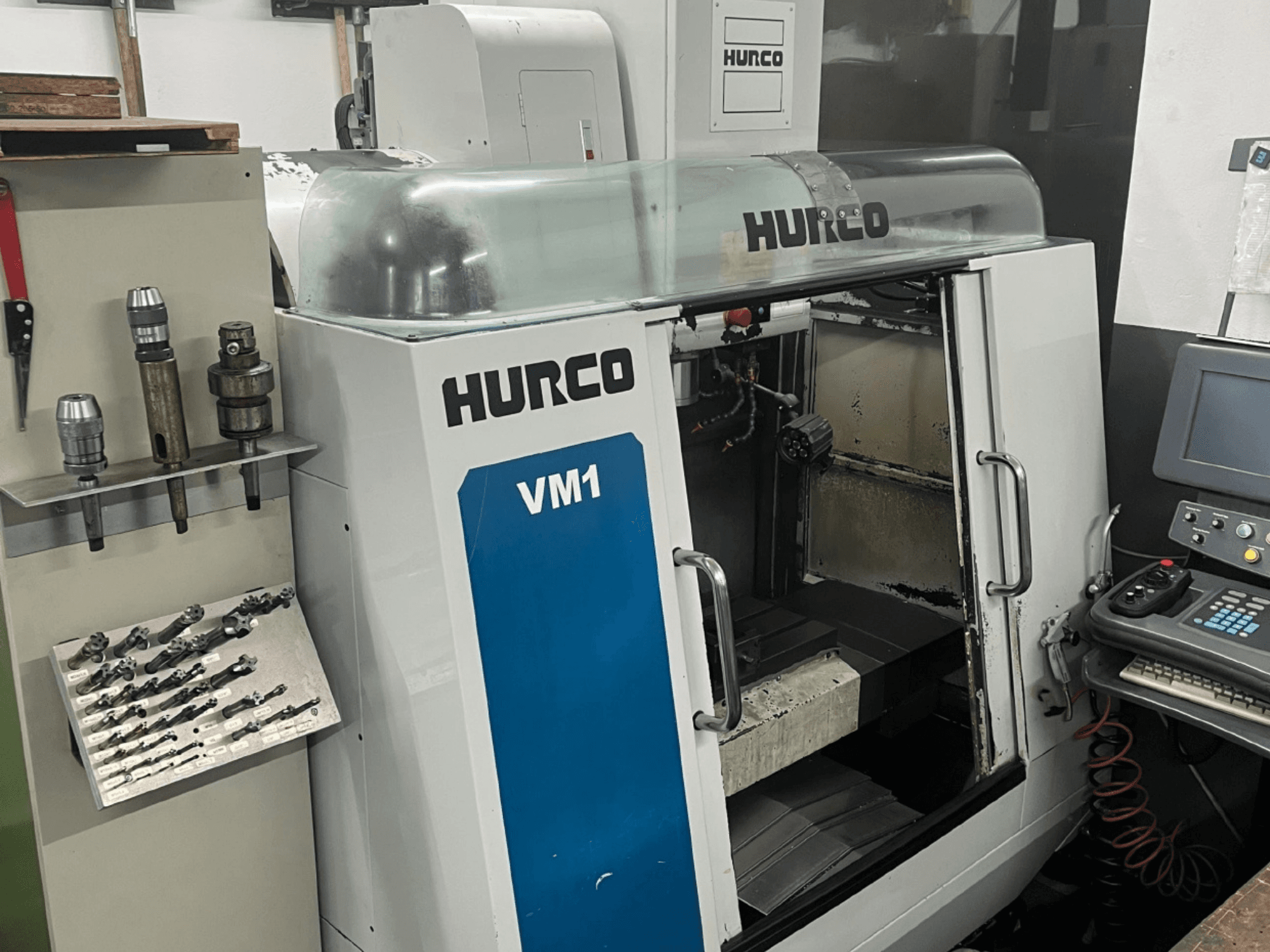Hurco VM1 vertikālais apstrādes centrs no priekšpuses, ar caurspīdīgu vāku, vadības paneli un uzstādītiem instrumentiem.