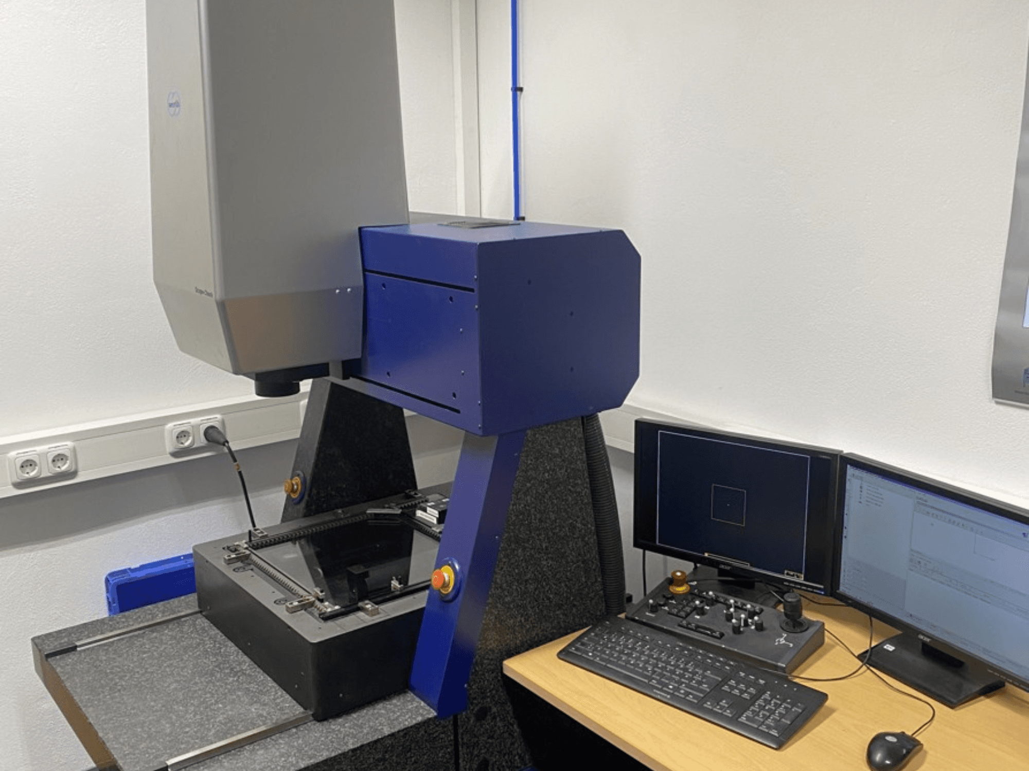 Werth Scope-Check 400 CMM laboratorijā, parādot mērīšanas galviņu un vadības paneli ar ekrāniem un tastatūru.