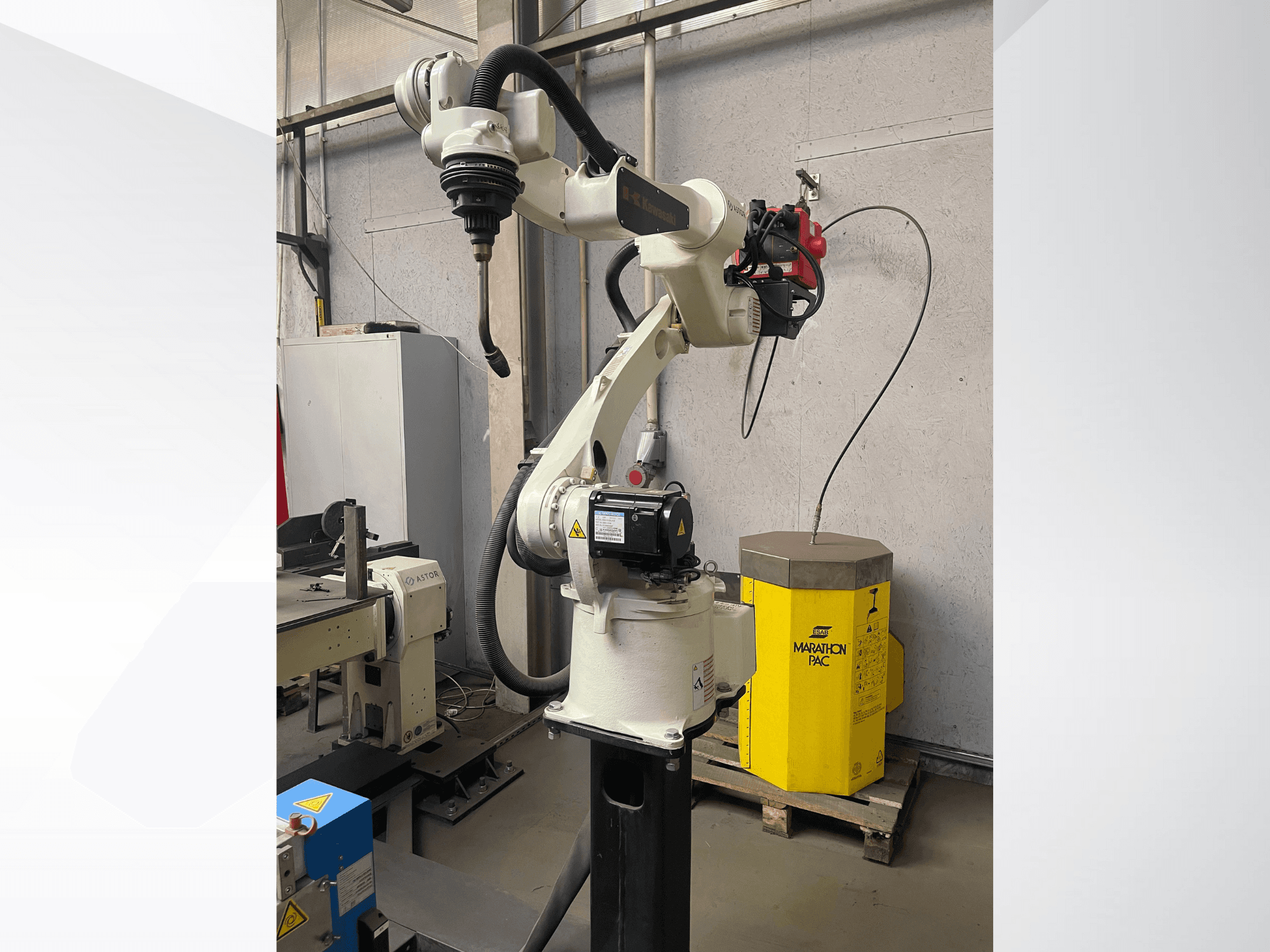 Kawasaki robotizētā roka no sānu skata ar uzstādītu instrumentu turētāju, fonā redzams dzeltens barošanas bloks.