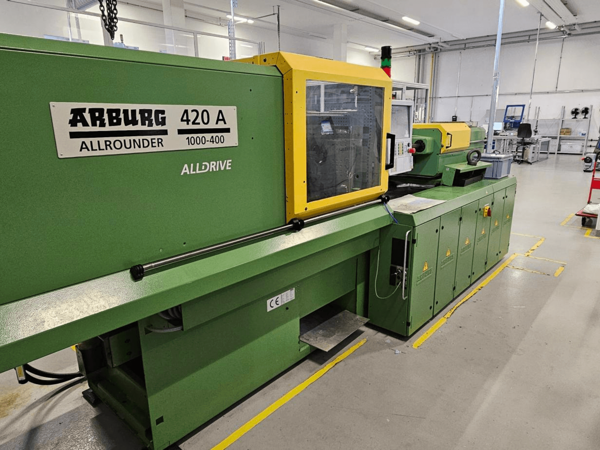 ARBURG 420 A Allrounder 1000-400, skats no priekšpuses; zaļa mašīna ar dzeltenu paneli, skārienekrānu un drošības funkcijām.