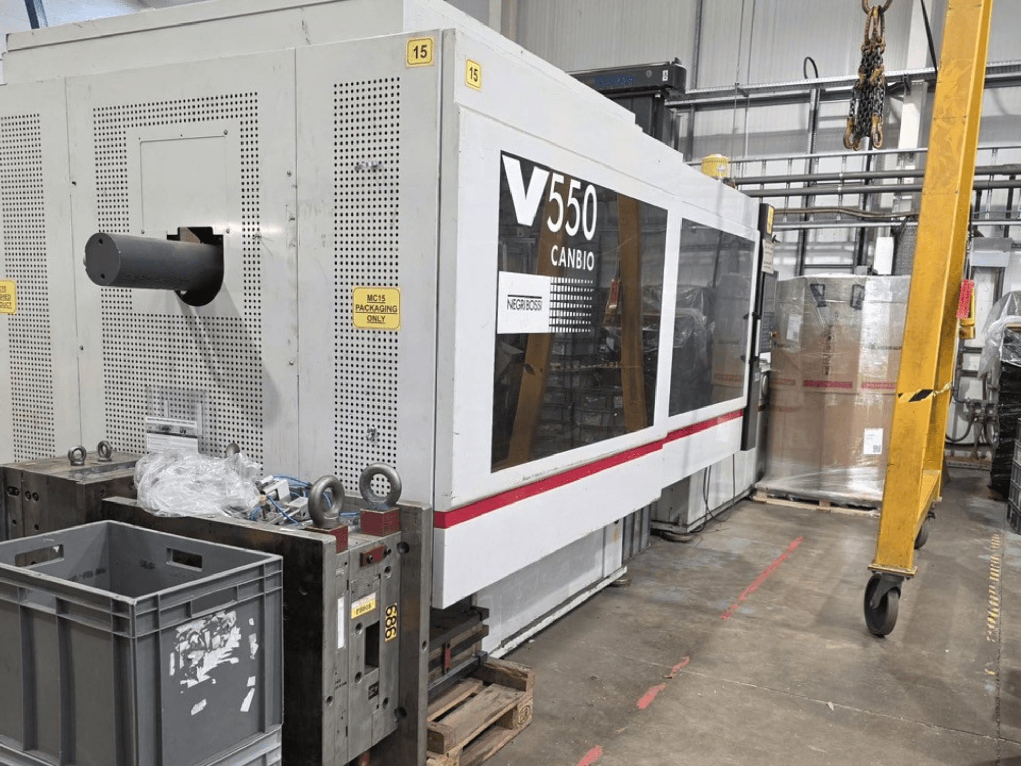 Negri Bossi V55000H-4250 hidrauliskā iesmidzināšanas iekārta, skats no sāniem, priekšplānā vadības panelis un pelēkas kastes.