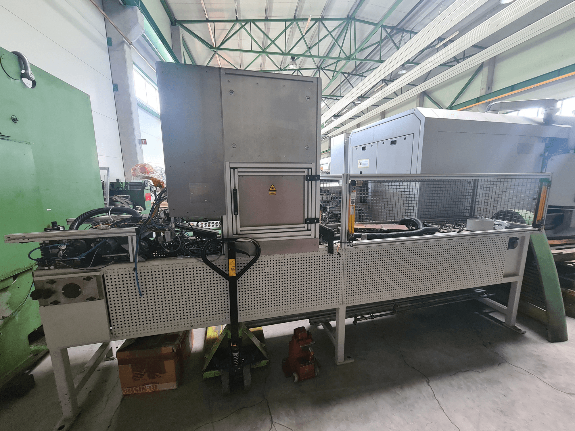 Rūpniecības iekārtas ar metāla rāmi, šļūtenēm un vadības paneli, skatoties no sāniem rūpnīcā.