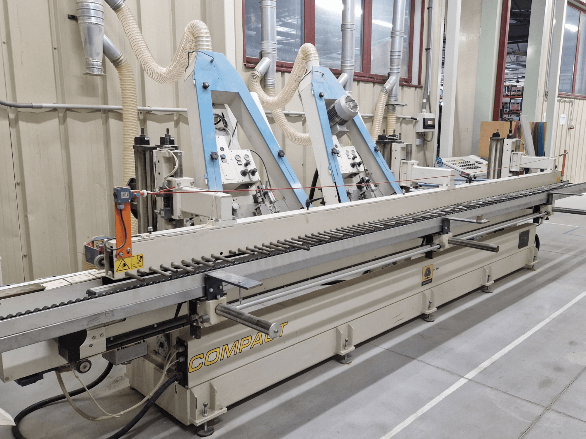 Lentes slīpmašīna TECNOLEGNO COMPACT 52 darbnīcā, redzams vadības panelis un slīpēšanas lentes mehānisms no sānu skata.