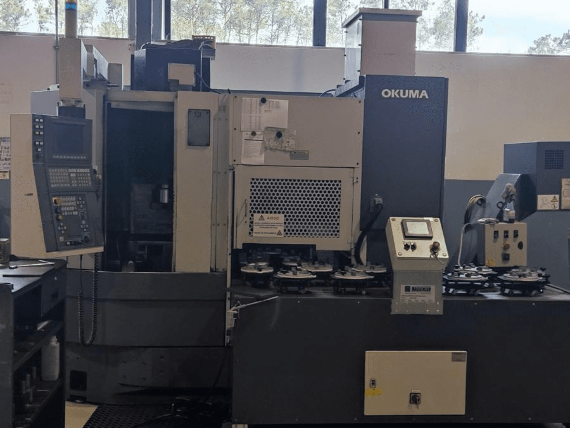 Okuma LVT300 vertikālās virpošanas darbgalds priekšpusē, ar vadības paneli, instrumentu turētājiem un apstrādes zonu.