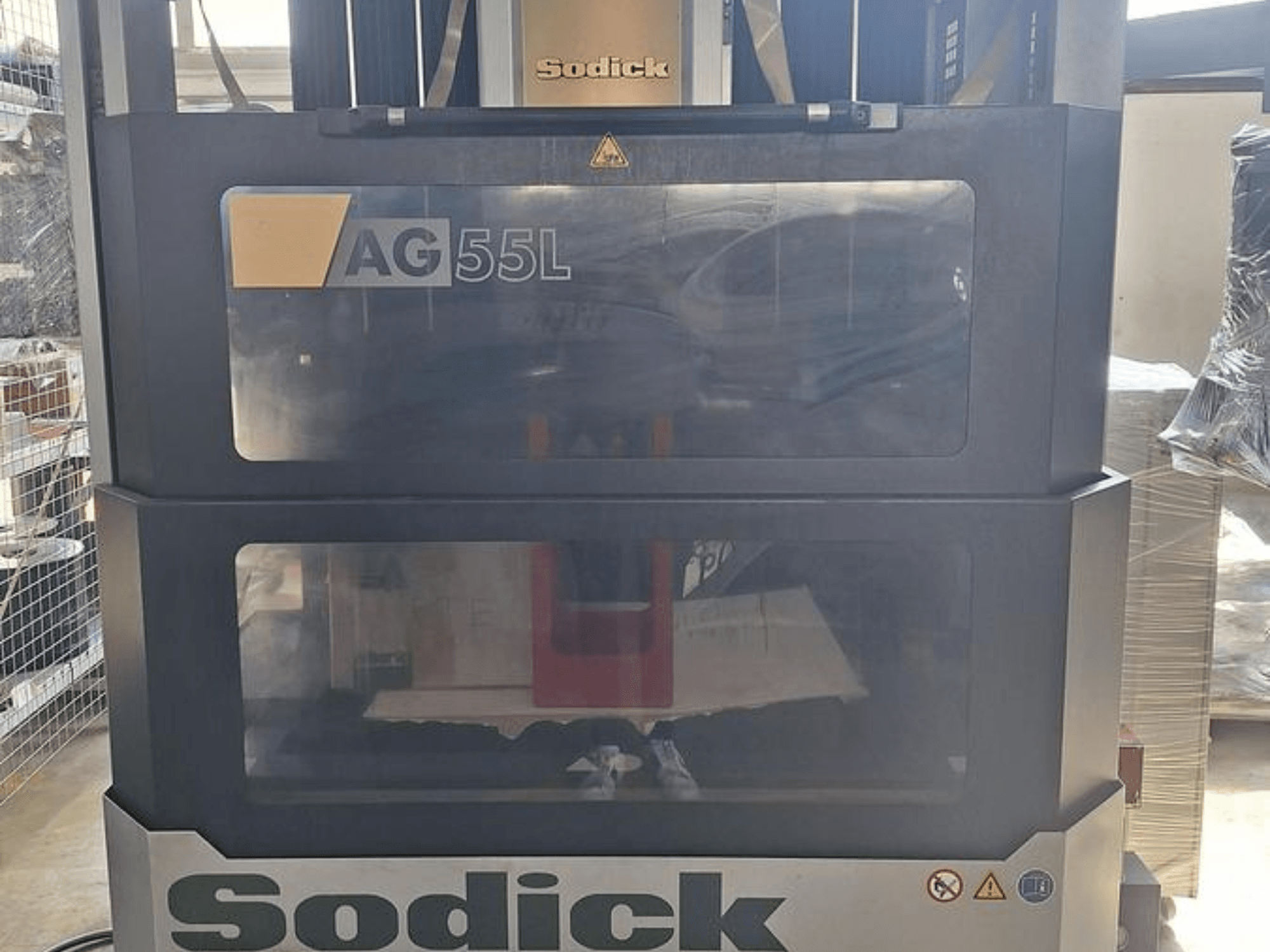 Sodick AG 55L štancēšanas EDM mašīna, priekšējais skats ar vadības elementiem, kas redzami caur caurspīdīgiem paneļiem, parādot darba vietu iekšpusē.
