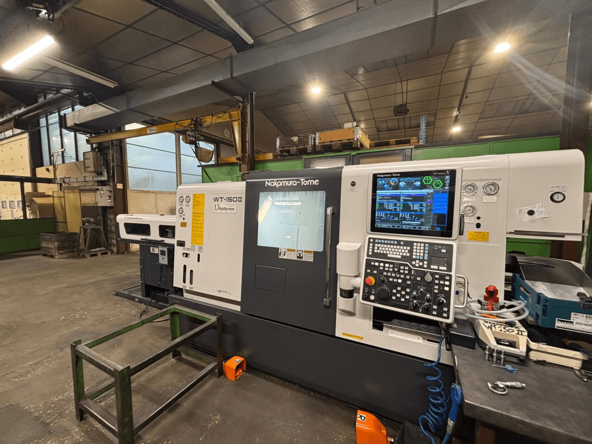 Nakamura-Tome WT-150II mašīna, skats no priekšpuses, ar vadības paneli un instrumentiem, kas redzami uz darbgalda darbnīcā.