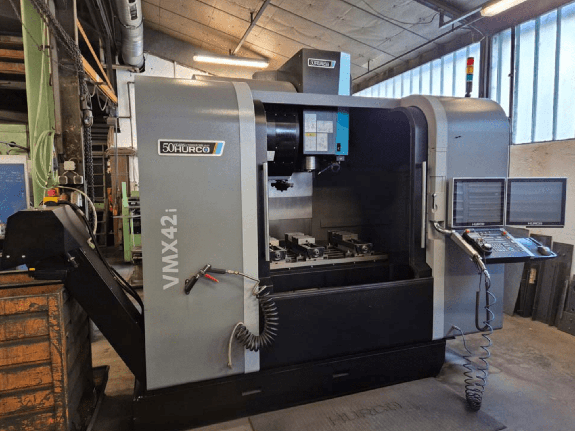 Hurco VMX 42i vertikālais apstrādes centrs, skats no priekšpuses, kurā redzams vadības panelis un darba zona ar skrūvēm.