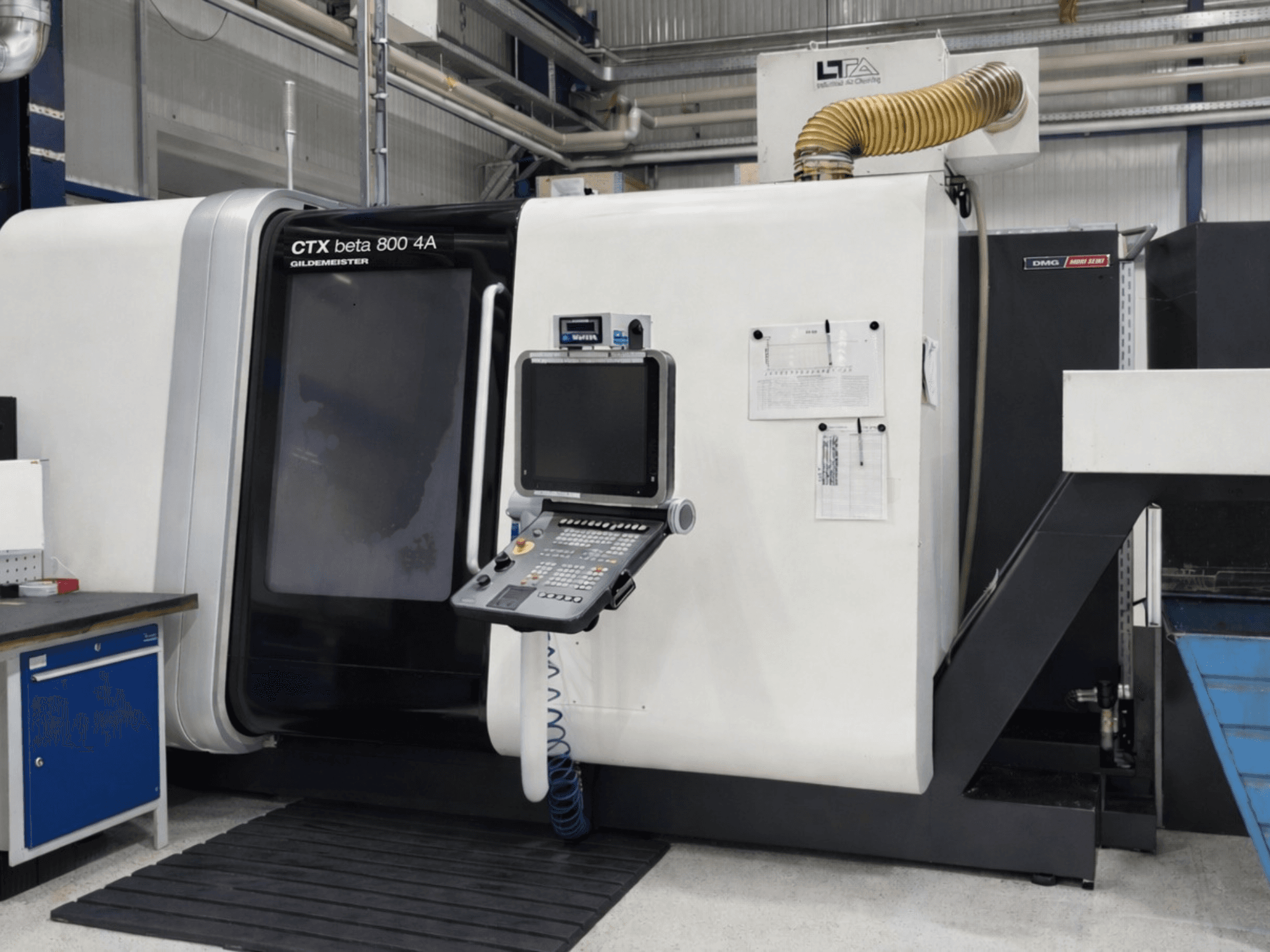 DMG CTX beta 800 4A daudzspindeles virpošanas stends, skats no priekšpuses, kurā redzams vadības panelis un ekspluatācijas dokumentācija.