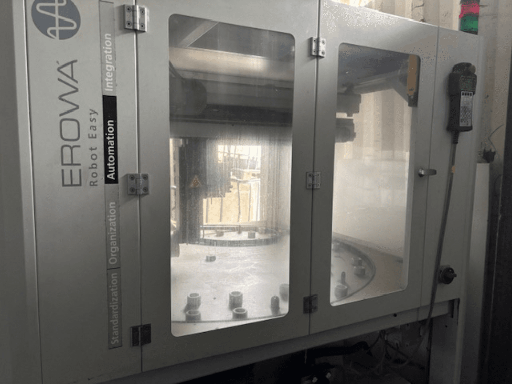 EROWA Robot Easy Automation priekšējais skats; caurspīdīgas durvis, redzami automatizācijas komponenti un vadības panelis.