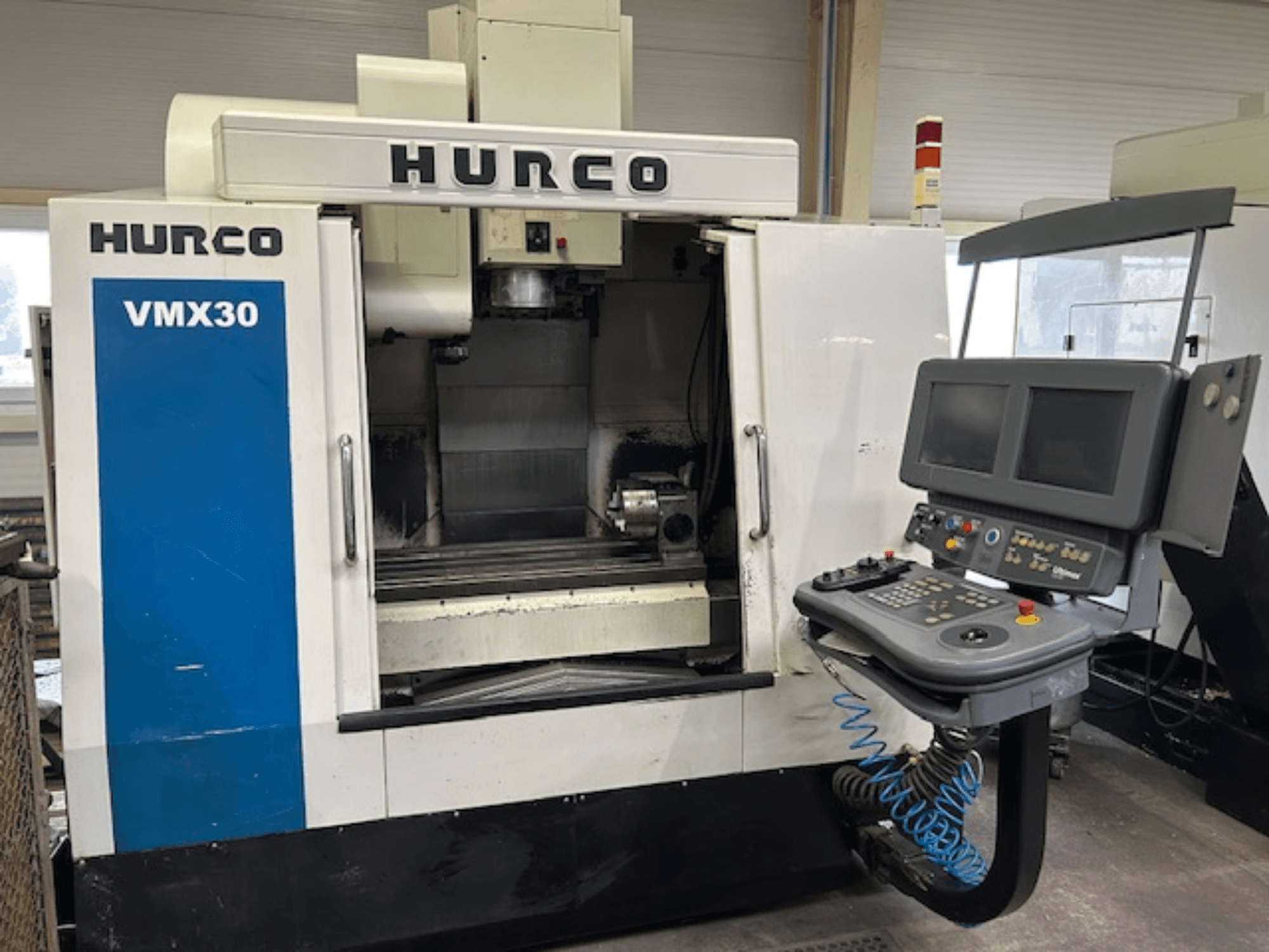 Hurco VMX30 CNC frēzmašīna darbnīcā, skats no priekšpuses; vadības panelis ar diviem ekrāniem un vadības pogām.