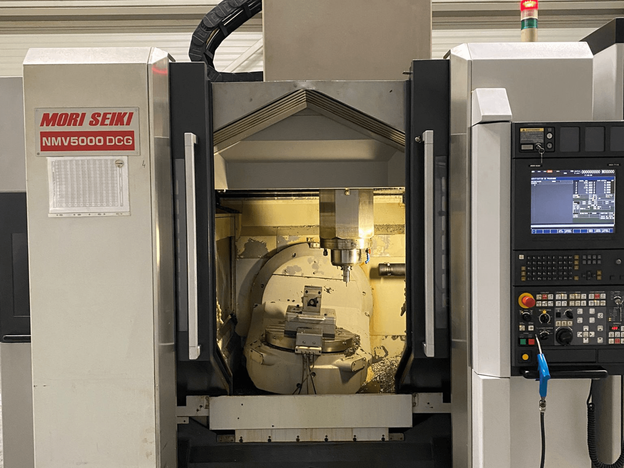 MORI SEIKI NMV 5000DCG universālais apstrādes centrs, priekšējais skats, kurā redzams vadības panelis un iekšējā apstrādes zona.