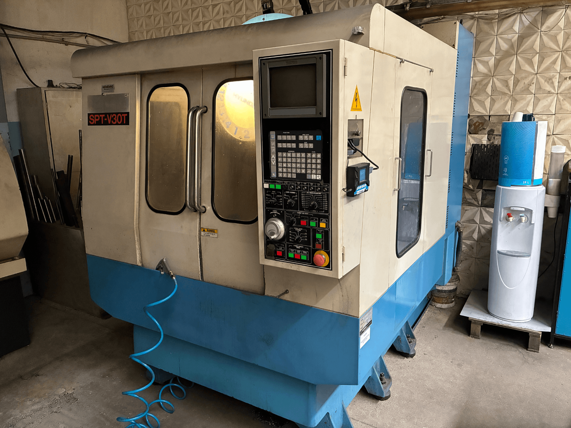 SPT-V30T CNC mašīna zilā un baltā krāsā, priekšējais skats, kurā redzams vadības panelis, durvis un gaisa šļūtene. Ideāli piemērots precīzai apstrādei.