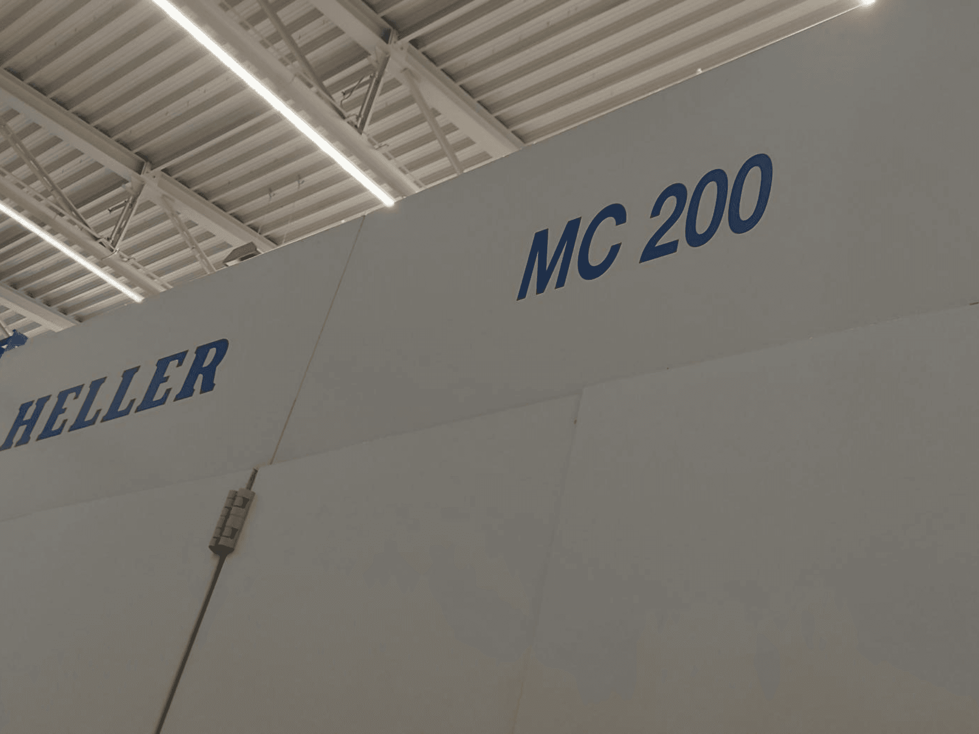 Heller MC 200 horizontālais apstrādes centrs, attēlots no sāniem, ar ziliem uzrakstiem uz baltas virsmas, izceļot zīmolu un modeli.