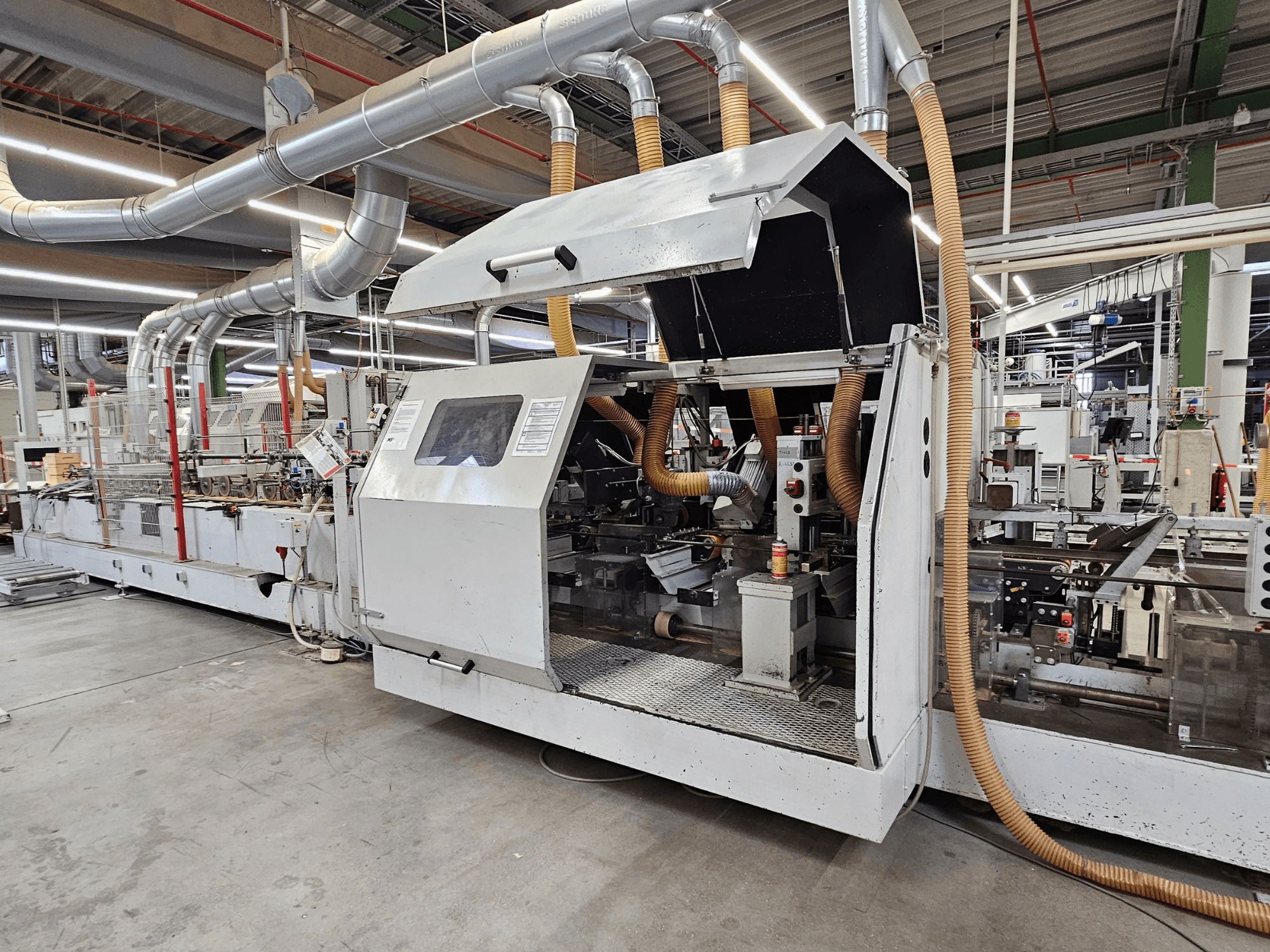 HOMAG FG63 slīpmašīna rūpnīcā, skats no sāniem, kurā redzami darba komponenti un putekļu nosūces sistēma.