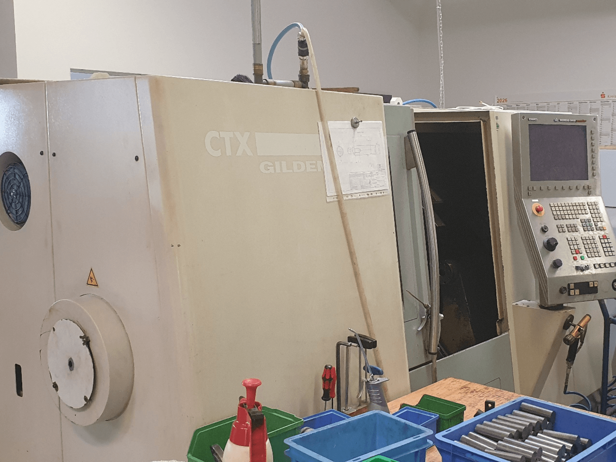 DMG GILDEMEISTER CTX 310 horizontālās virpošanas mašīnas skats no priekšpuses, redzams vadības panelis, priekšplānā — instrumenti un konteineri.