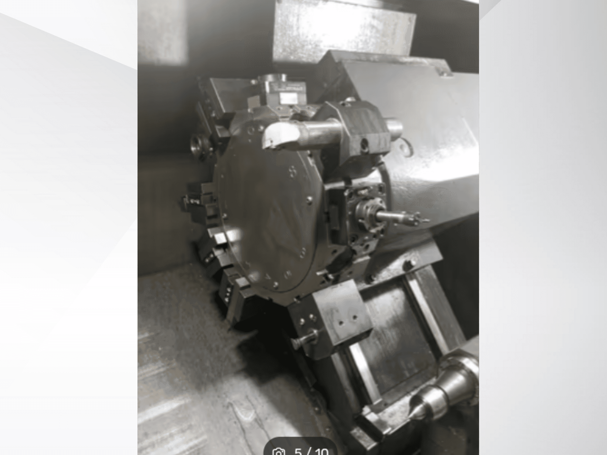 Precīzas mašīnas detaļas tuvplāns, kurā redzami zobrati un metāla detaļas, skatoties no leņķa perspektīvas. Nav redzams zīmols.