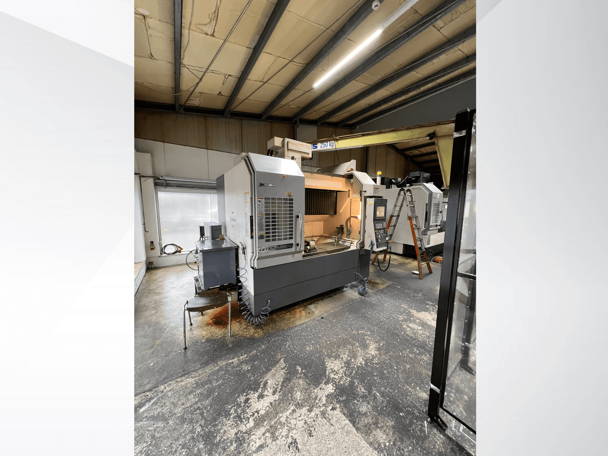 GRETOS 750 CNC darbnīcā, skats no priekšpuses, redzams vadības panelis un darba zona ar instrumentiem, fonā redzamas kāpnes.