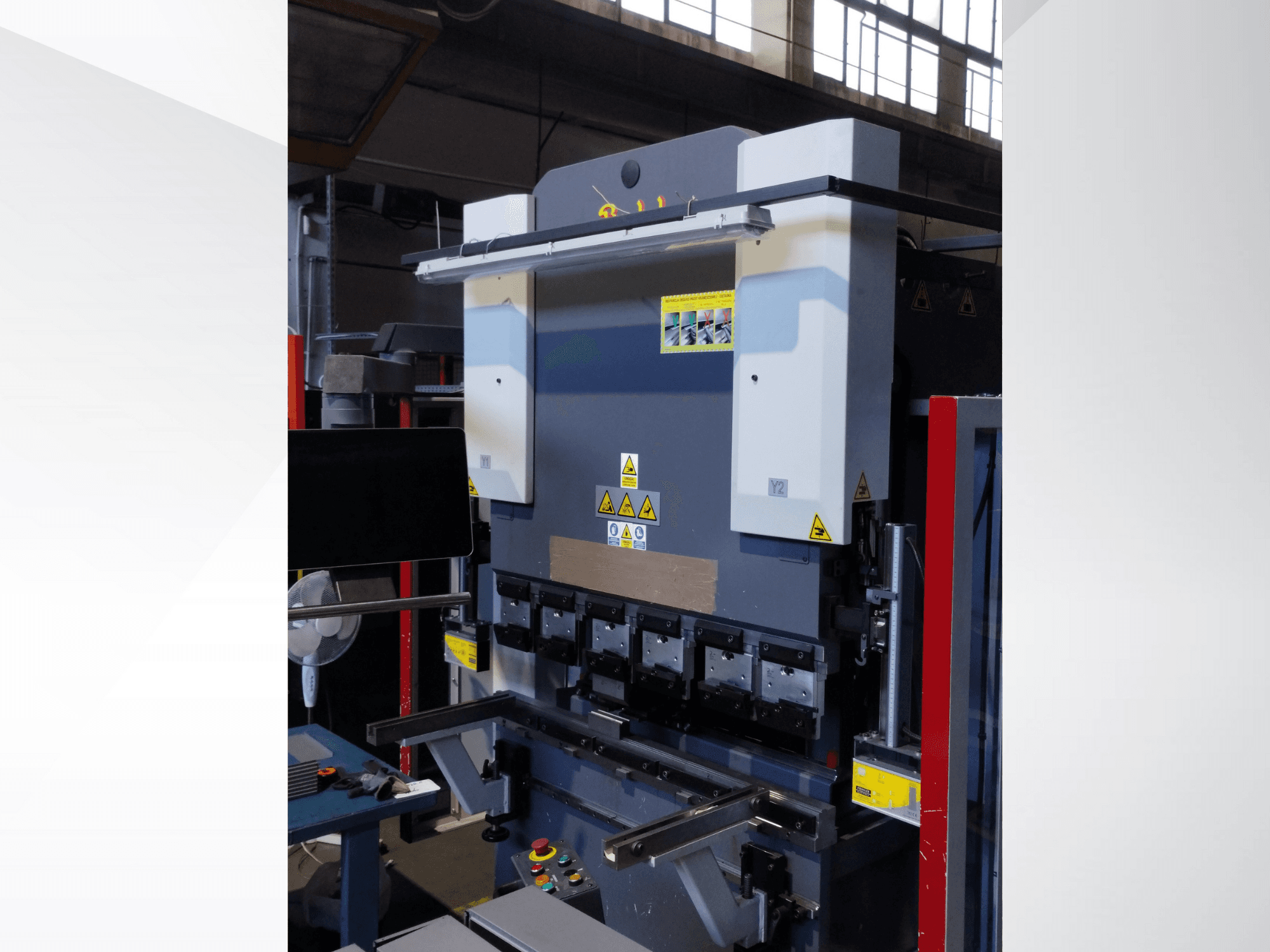 Preses bremžu iekārta, skats no priekšpuses. Redzamas vadības ierīces, drošības uzlīmes un vairāki presformu turētāji precīzai liešanai.