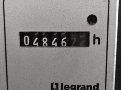 Legrand stundu skaitītājs ar rādījumu 048467.6, priekšējais skats ar sarkanu indikatora gaismu un melniem cipariem uz teksturēta gaiša fona.