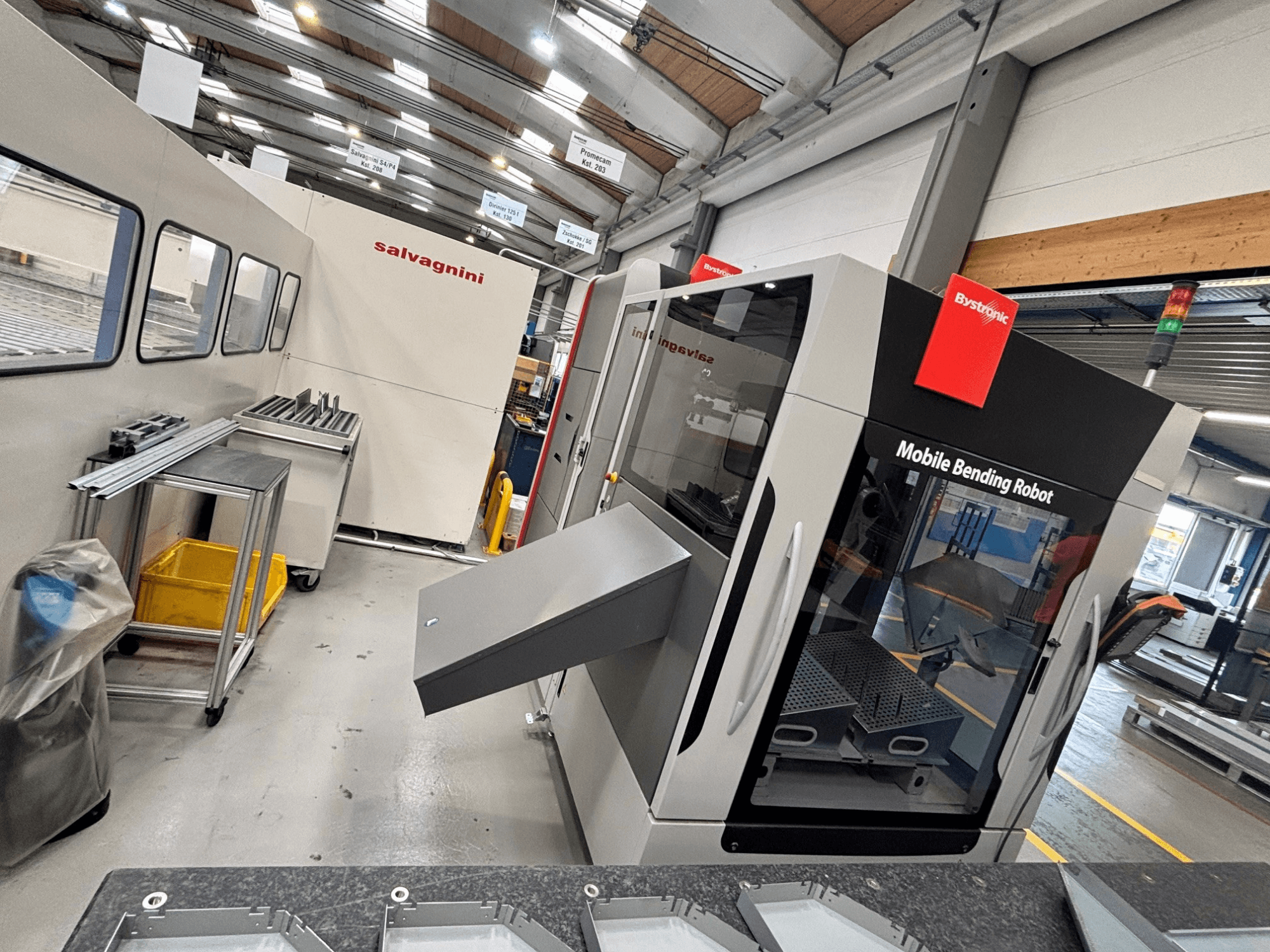 Bystronic Xpert 40/1030 lieces preses priekšskats, kurā redzams mobilais lieces robots un darba zona ar metāla detaļām uz galda.