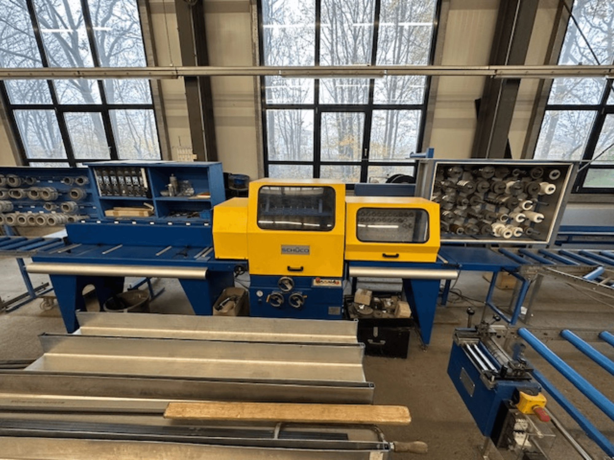 Skats uz SCHÜCO ISOMAT 4 darbgaldiem ar dzeltenu vadības paneli, vairākiem ruļļiem un glabāšanas nodalījumu.