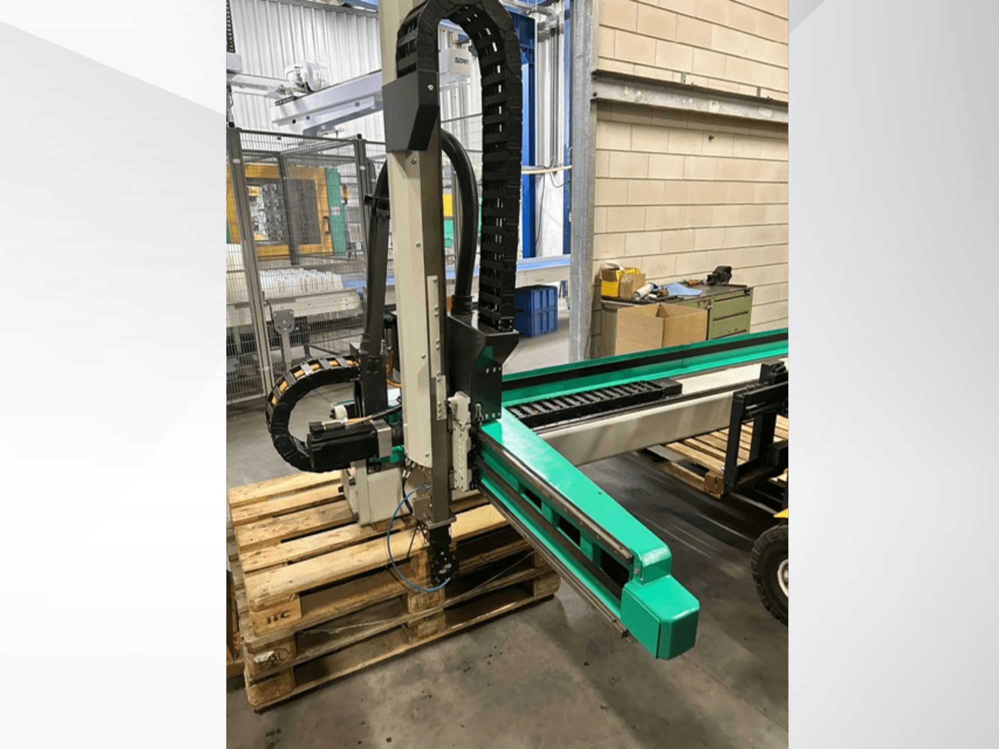 Arburg Multilift Select 15kg quer, skats no malas uz koka paliktņiem, redzama robota roka un vadības komponenti.