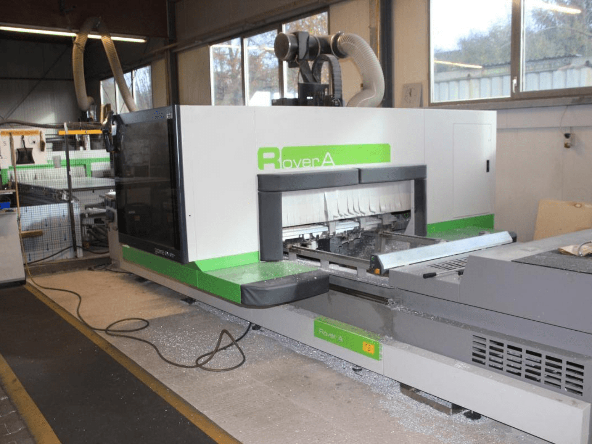 BIESSE Rover A 1232 CNC frēzētājs, skats no sāniem, kurā redzama griešanas zona un vadības panelis rūpnieciskā vidē.