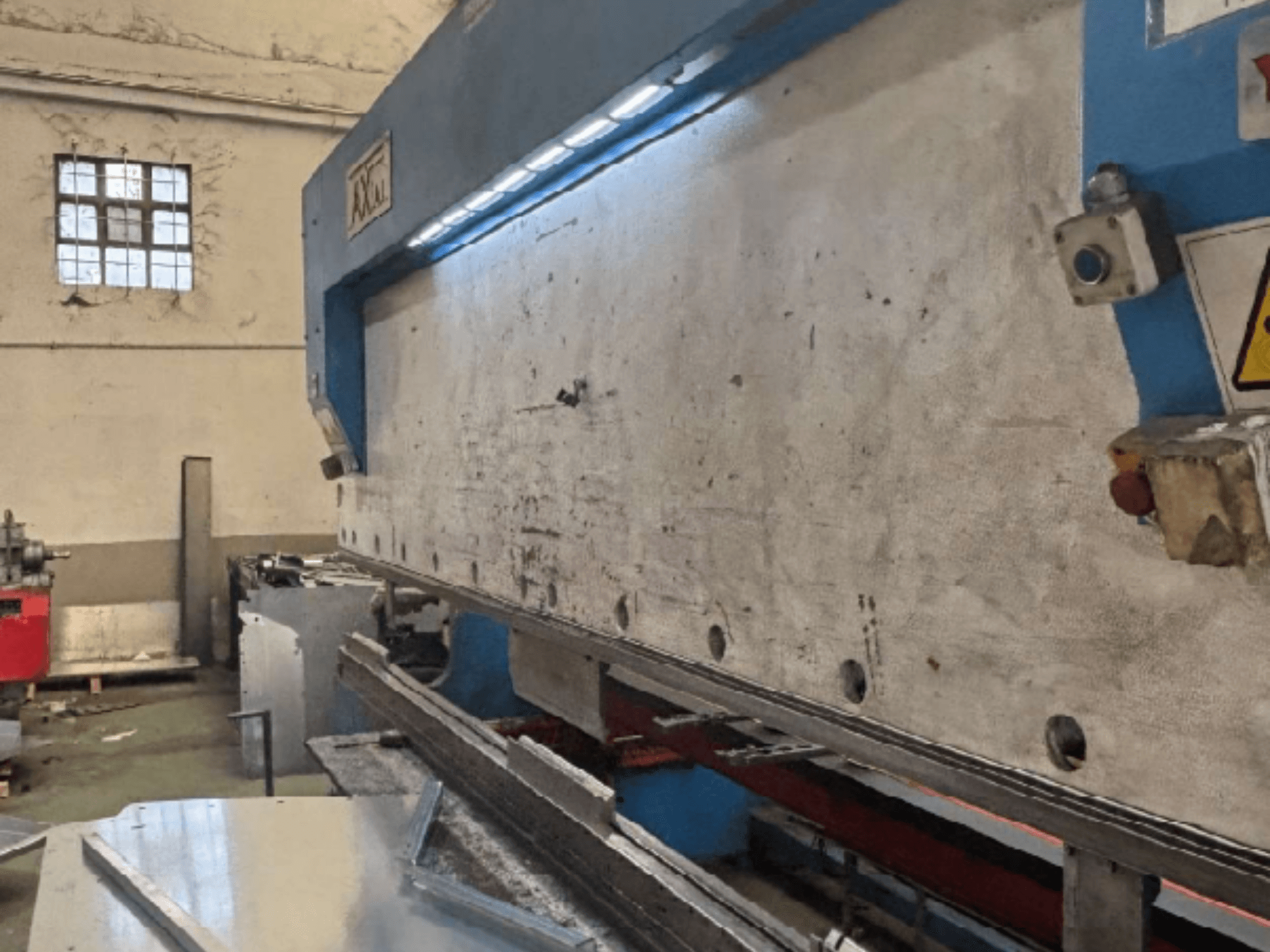 Axial PHS-W-124 palešu pārvietošanas sistēma darbnīcā, sānu skats, kurā redzama darba virsma un vadības paneļa detaļas.