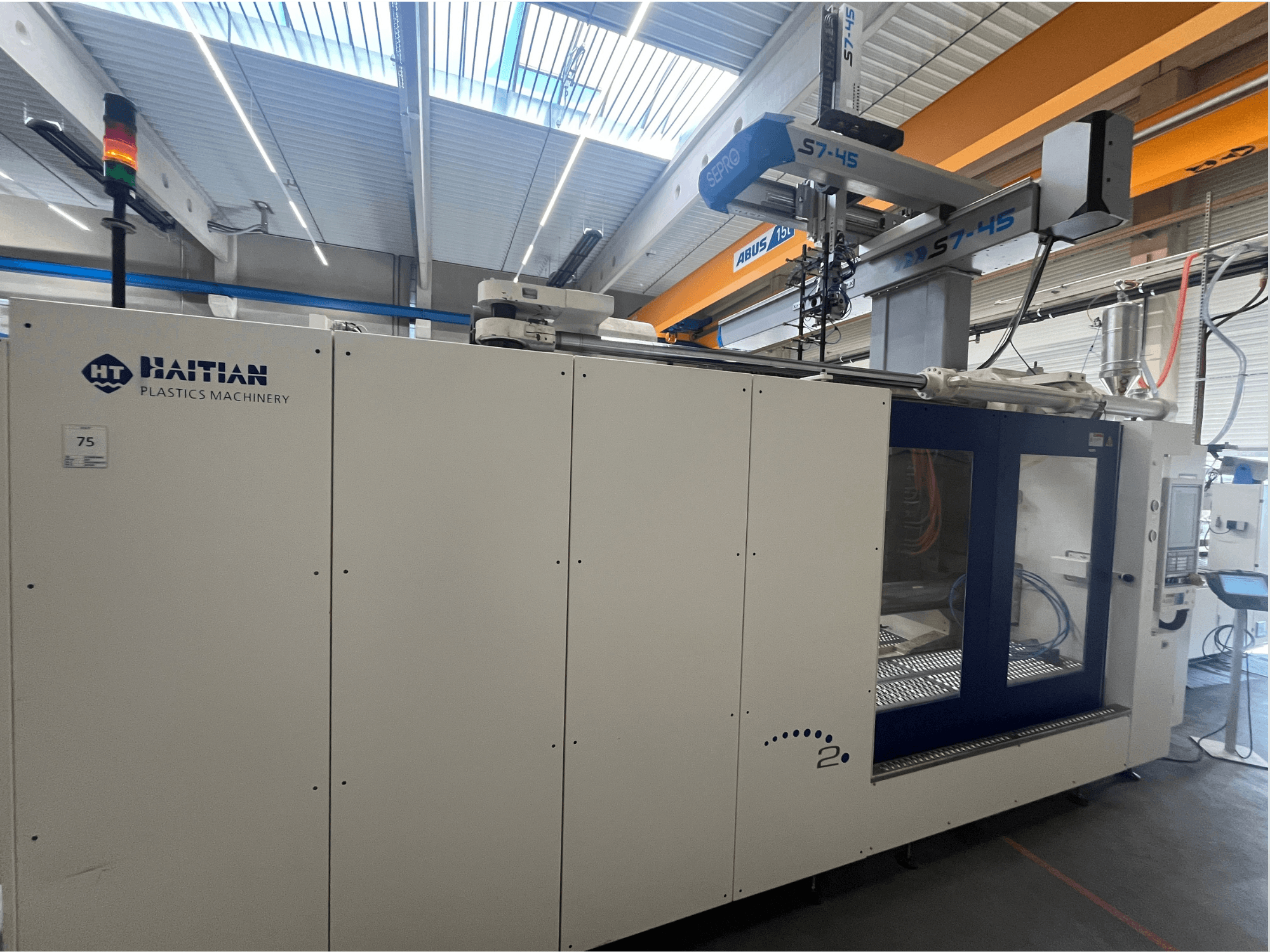 Haitian S7-45 iesmidzināšanas liešanas mašīna sānu skatā ar vadības paneli un drošības gaismas indikatoru. Balts un zils dizains.