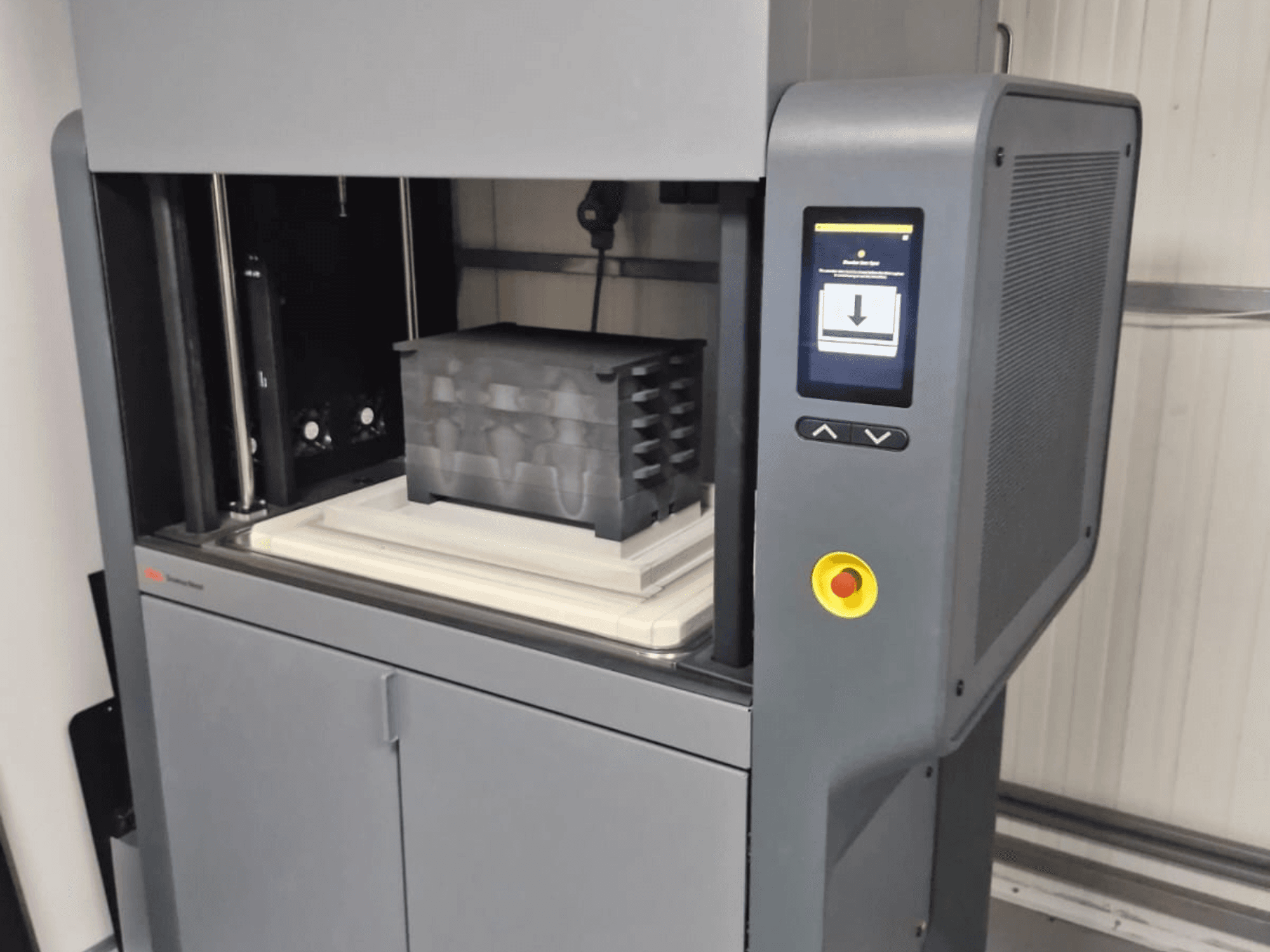 Desktop Metal 3D printeris Metal Studio 2, priekšējais skats, kurā redzams vadības panelis un drukas gulta ar melnu konteineru.