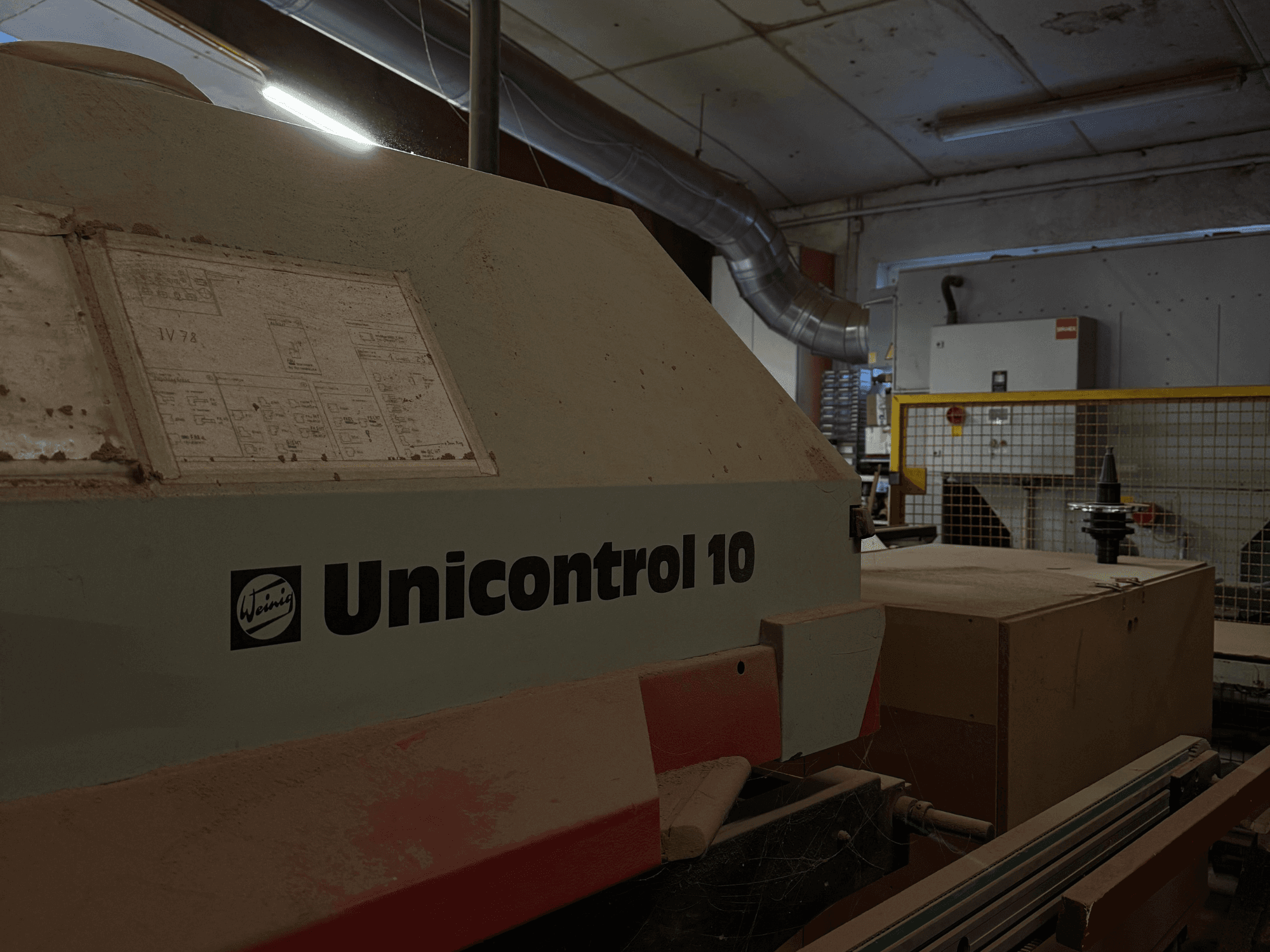 Weinig Unicontrol 10 mašīna no sānu leņķa, putekļaina virsma, uz priekšējā paneļa redzamas tehniskās shēmas.